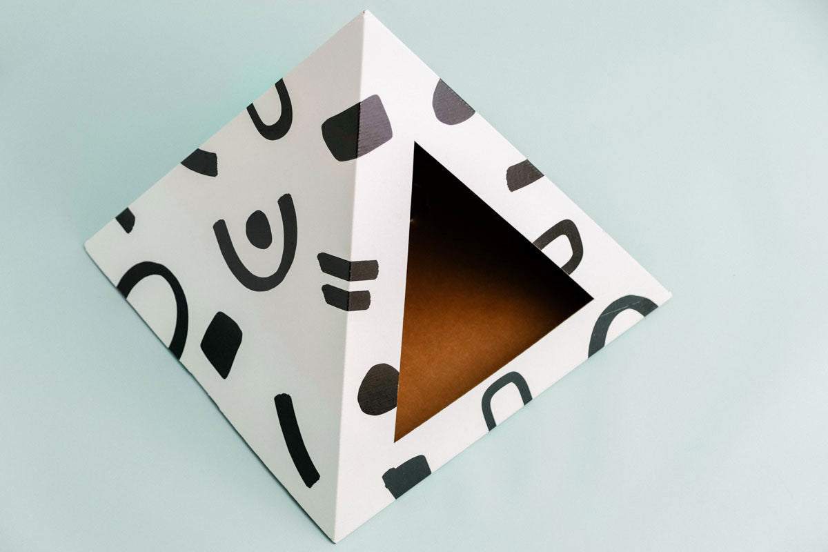Modern cardboard cat pyramid with black abstract doodle patterns and triangular entrance.