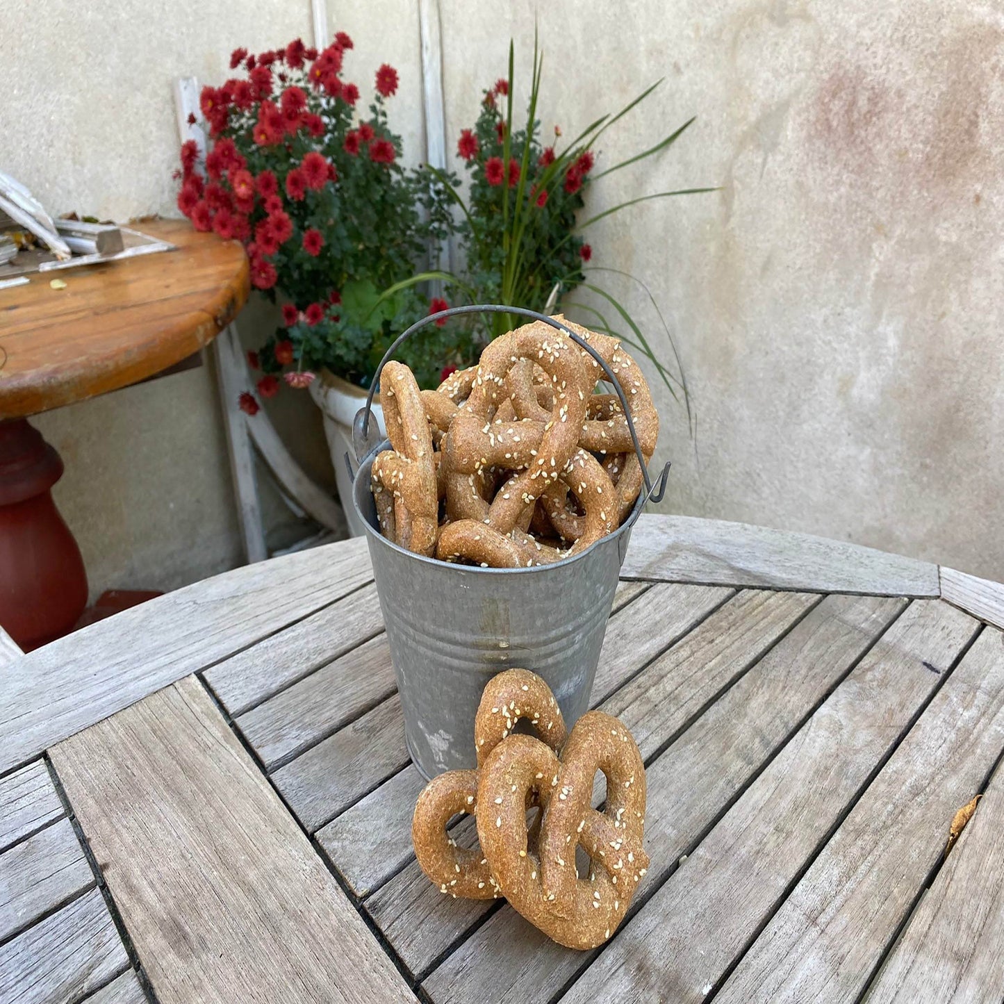 Bucket of organic parmesan pretzels dog treats on wooden table with red flowers in background