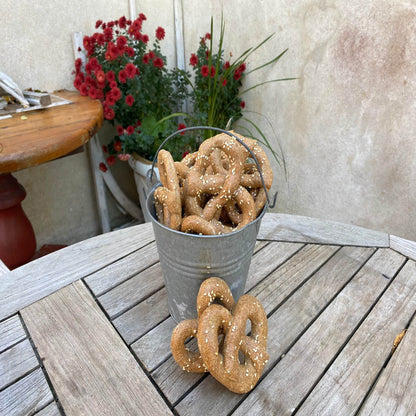 Bucket of organic parmesan pretzels dog treats on wooden table with red flowers in background