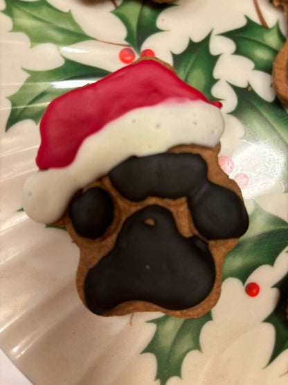 Santa Paws Organic Dog Treats shaped like a paw print with black and brown cookie base topped with red and white Santa hat icing