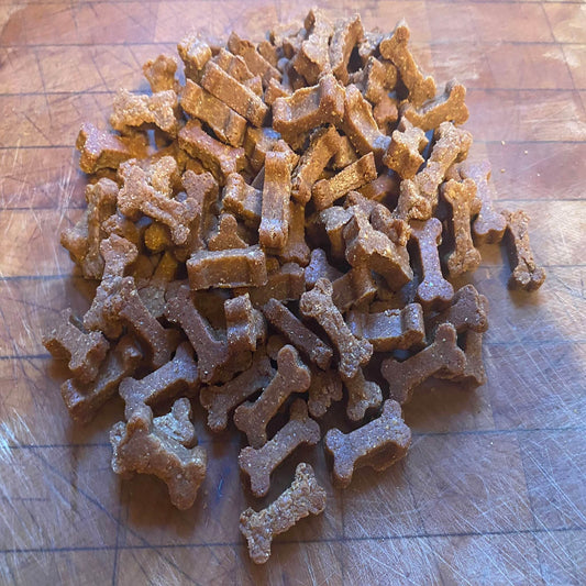 Peanut butter organic dog training treats shaped like small bones on a wooden surface