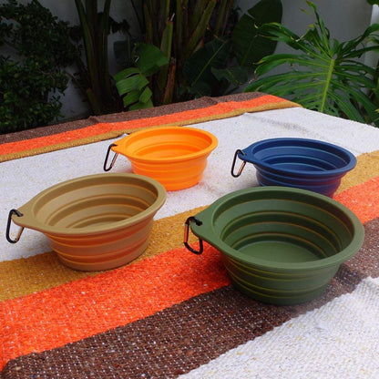 Colorful collapsible pet bowls with clips arranged on a textured outdoor surface